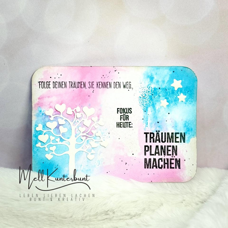 Eine lebendige Karte mit einer weißen Baumsilhouette aus der Stanzschablone: Baum mit Herzen von Stanzenshop.de, mit Sternausschnitten und deutschem Motivationstext auf blau-rosa Aquarellhintergrund - ideal für Scrapbooking oder Bastelzubehör.