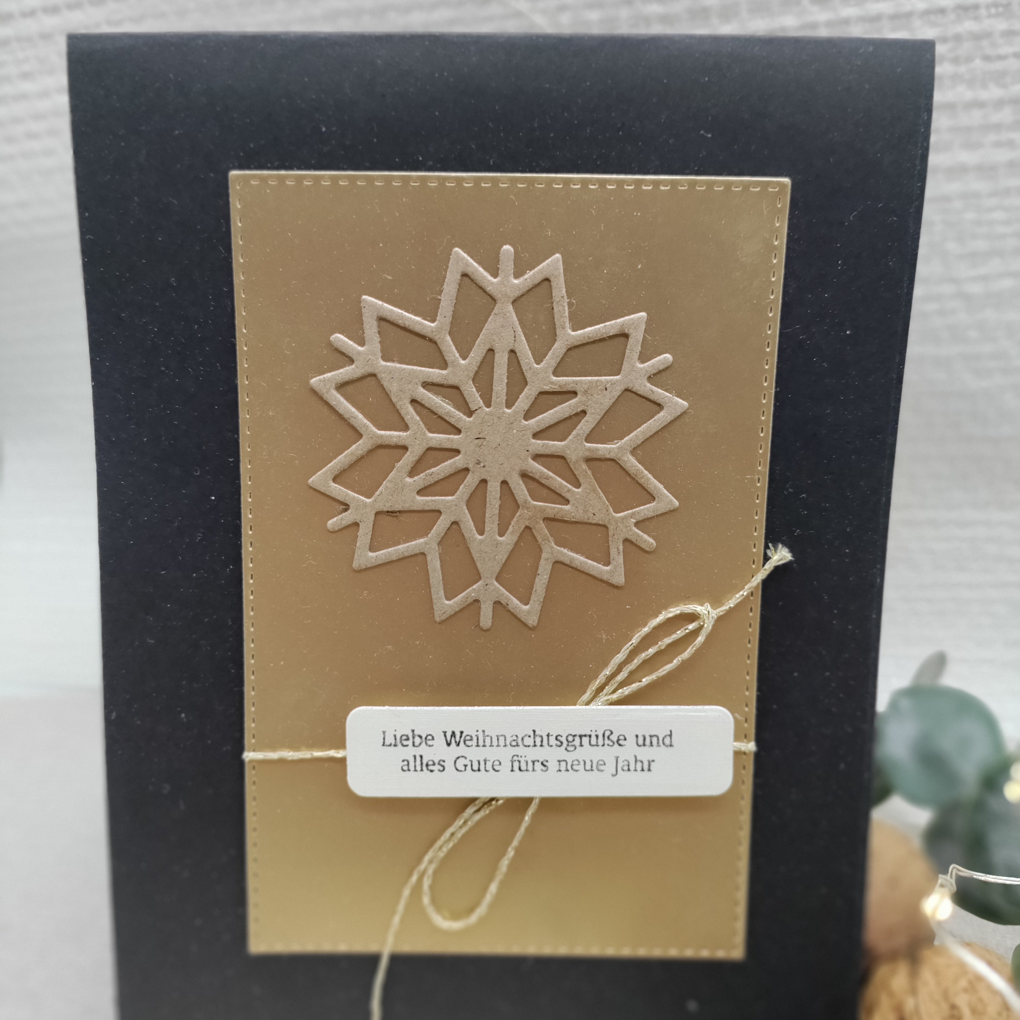 Eine schwarz-goldene Weihnachtskarte mit einer großen Schneeflocke, die mit der Stanzschablone ausgeschnitten wurde: Schneekristall von Stanzenshop.de und einem deutschen Weihnachtsgruß-Etikett, das mit einer goldenen Schnur gebunden ist.