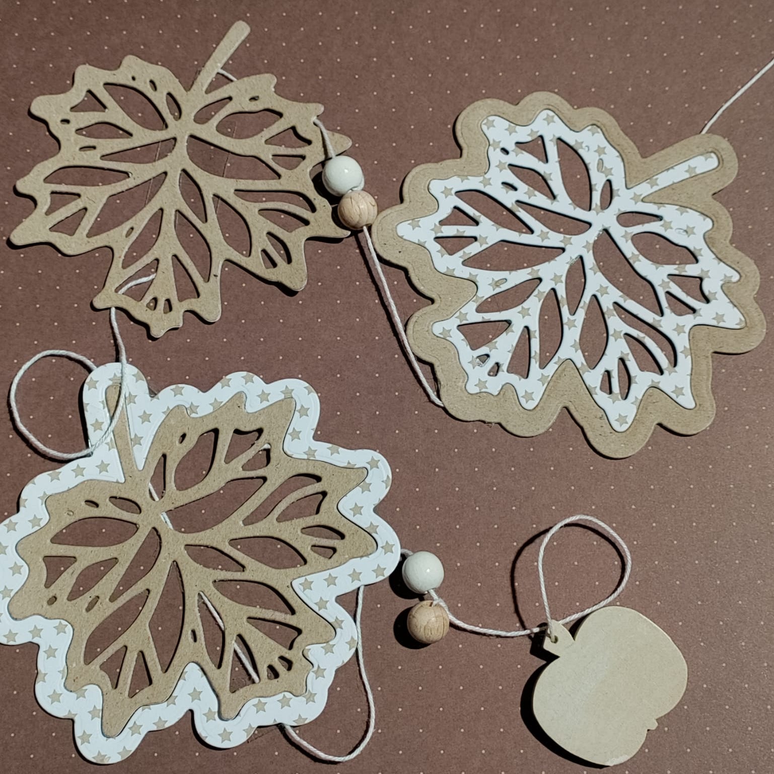 Die "Stanzschablone: Blatt mit Rahmen" von Stanzenshop.de zeigt Blattausschnitte mit Rahmen, ideal zum Basteln oder Scrapbooking, wunderschön in Szene gesetzt mit Holzakzenten auf einem braun gepunkteten Hintergrund.