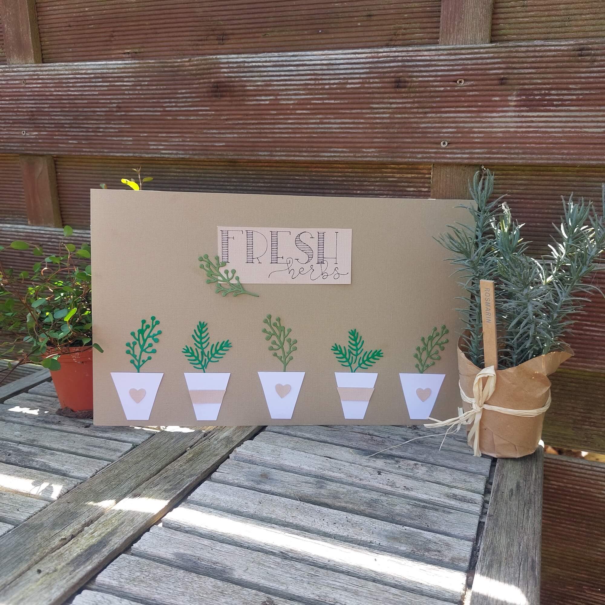 Ein handgemachtes "Frische Kräuter"-Schild mit Pflanzenausschnitten aus der Stanzenschablone Perlenzweige von Stanzenshop.de steht auf einem Holztisch neben zwei Kräutertöpfen - perfekt zum Basteln oder Scrapbooking.