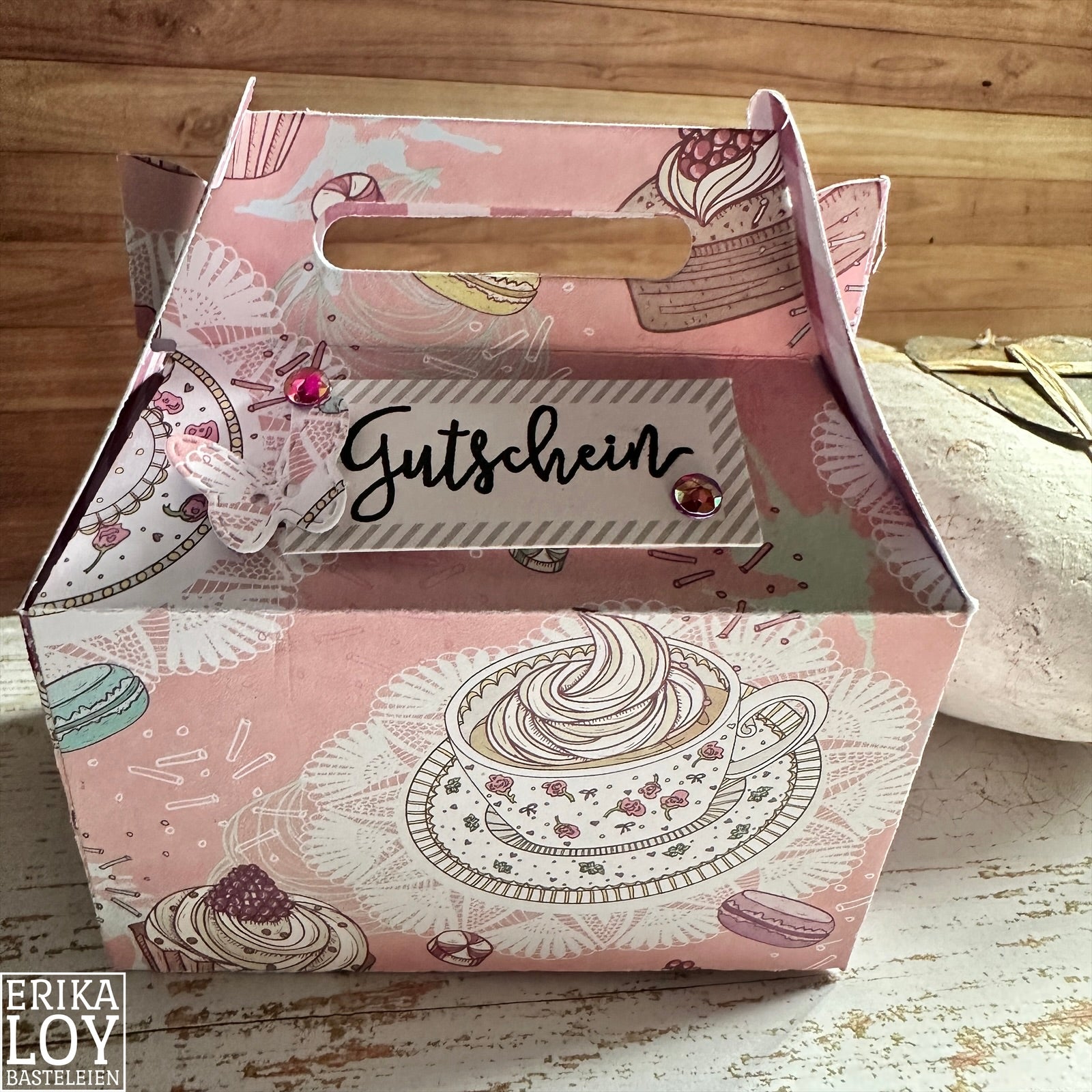 Die "Stanzschablone Große Schachtel" von Stanzenshop.de ist eine rosa Deko-Papierschachtel mit Teetassen- und Dessertmotiven, einem "Gutschein"-Etikett und Pailletten-Akzenten - ideal für Basteln oder Gastgeschenke.