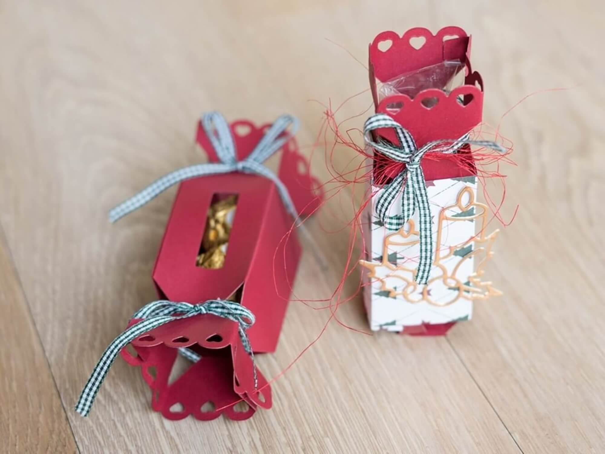 Zwei rote handgefertigte Geschenkschachteln aus der Stanzschablone Schachtel in Bonbonform von Stanzenshop.de mit Wellenkanten und Schleifenband, präsentiert auf einer hellen Holzfläche - ideale Gastgeschenke für besondere Anlässe.