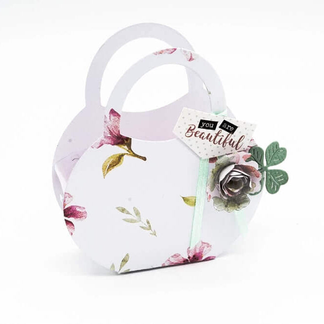 Die Stanzschablone Bastelset Handtasche von Stanzenshop.de ist eine dekorative Papiertasche in Handtaschenform mit floralen Mustern, einer Papierblume und einem "You are Beautiful"-Anhänger - ideal für Scrapbooking oder zum Kombinieren mit Ihren Lieblings-Stanzschablonen.