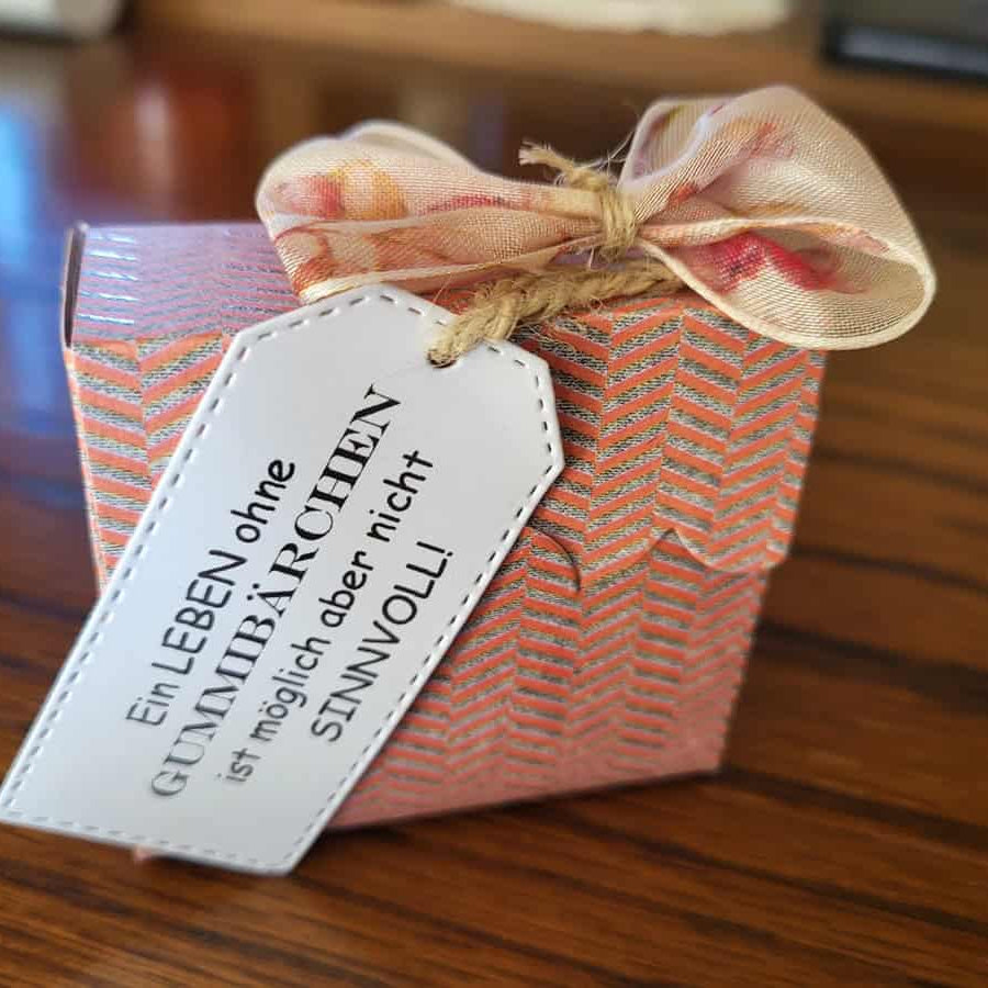 Die "Stanzschablone Schilder in fünf verschiedenen Größen" von Stanzenshop.de liegt auf Holz - ideal zum Basteln oder Scrapbooking, mit rosa Muster, Schleife und einem weißen Etikett mit deutschem Text.