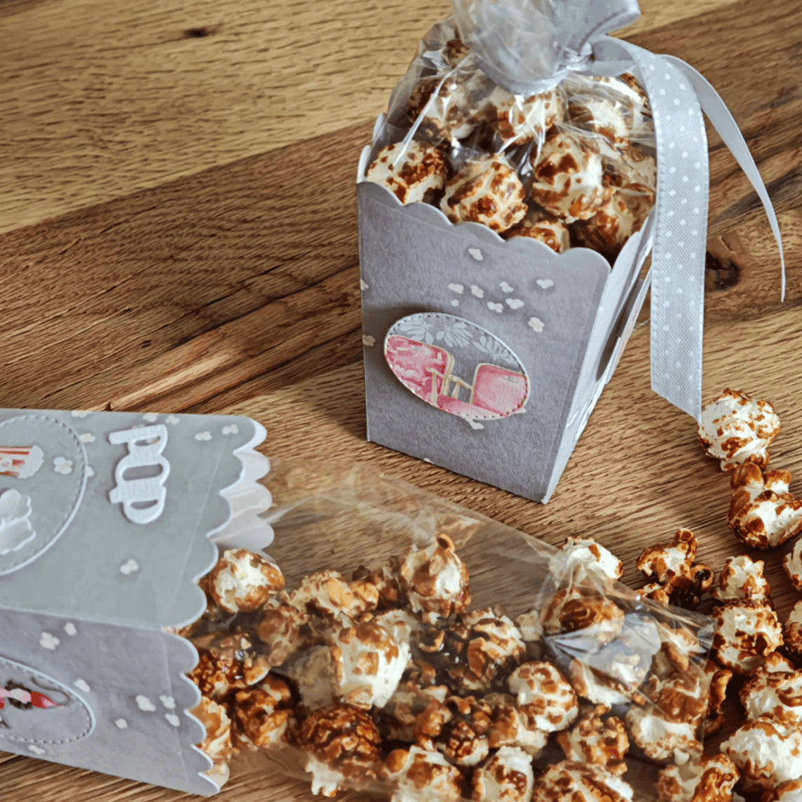 Zwei Karamell-Popcornschachteln - eine aufrecht mit Schleife, die andere Popcorn verschüttend - zeigen kreative Möglichkeiten, die Stanzschablone Popcornschachtel von Stanzenshop.de zu verwenden. Ideal als Gastgeschenke zur Hochzeit oder zum Basteln von Schachteln.