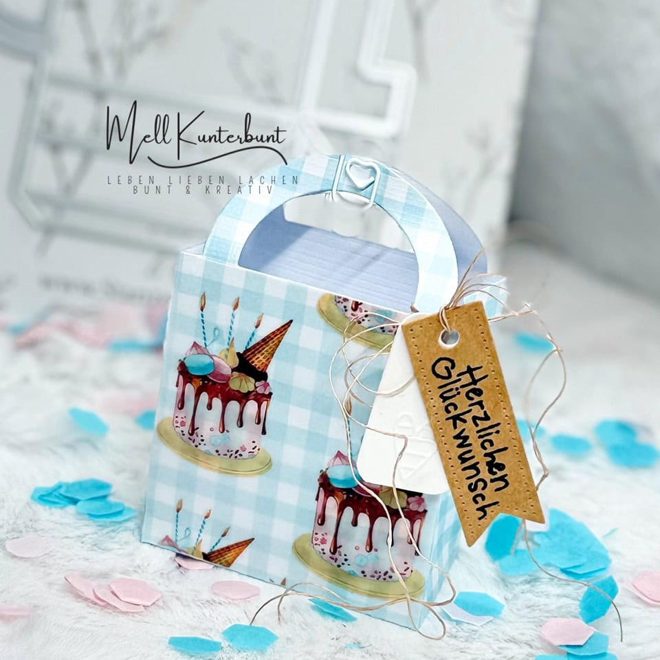 Die Stanzschablone Kleine Tasche von Stanzenshop.de fertigt eine kleine Tasche mit Kuchenmotiv und braunem "Herzlichen Glückwunsch"-Anhänger, umgeben von blau-pinkem Konfetti - ideal zum Basteln oder als Geschenkverpackung.