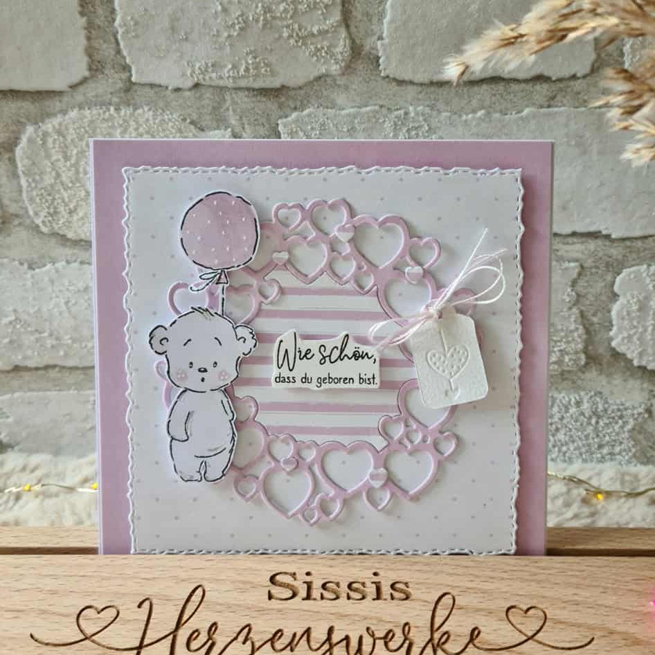 Handgefertigte Karte mit der Stanzenshop.de Stanzschablone Kreis aus Herzen, mit einem Bären, der einen Luftballon hält und dem Spruch "Wie schön, dass du geboren bist" auf rosa-weißem Hintergrund - ideal für Basteln-Fans.