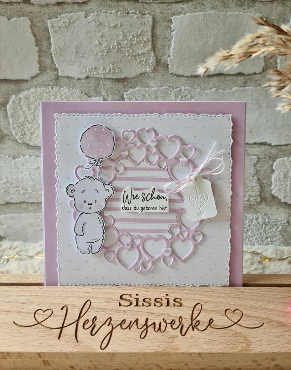 Handgefertigte Karte mit der Stanzenshop.de Stanzschablone Kreis aus Herzen, mit einem Bären, der einen Luftballon hält und dem Spruch "Wie schön, dass du geboren bist" auf rosa-weißem Hintergrund - ideal für Basteln-Fans.
