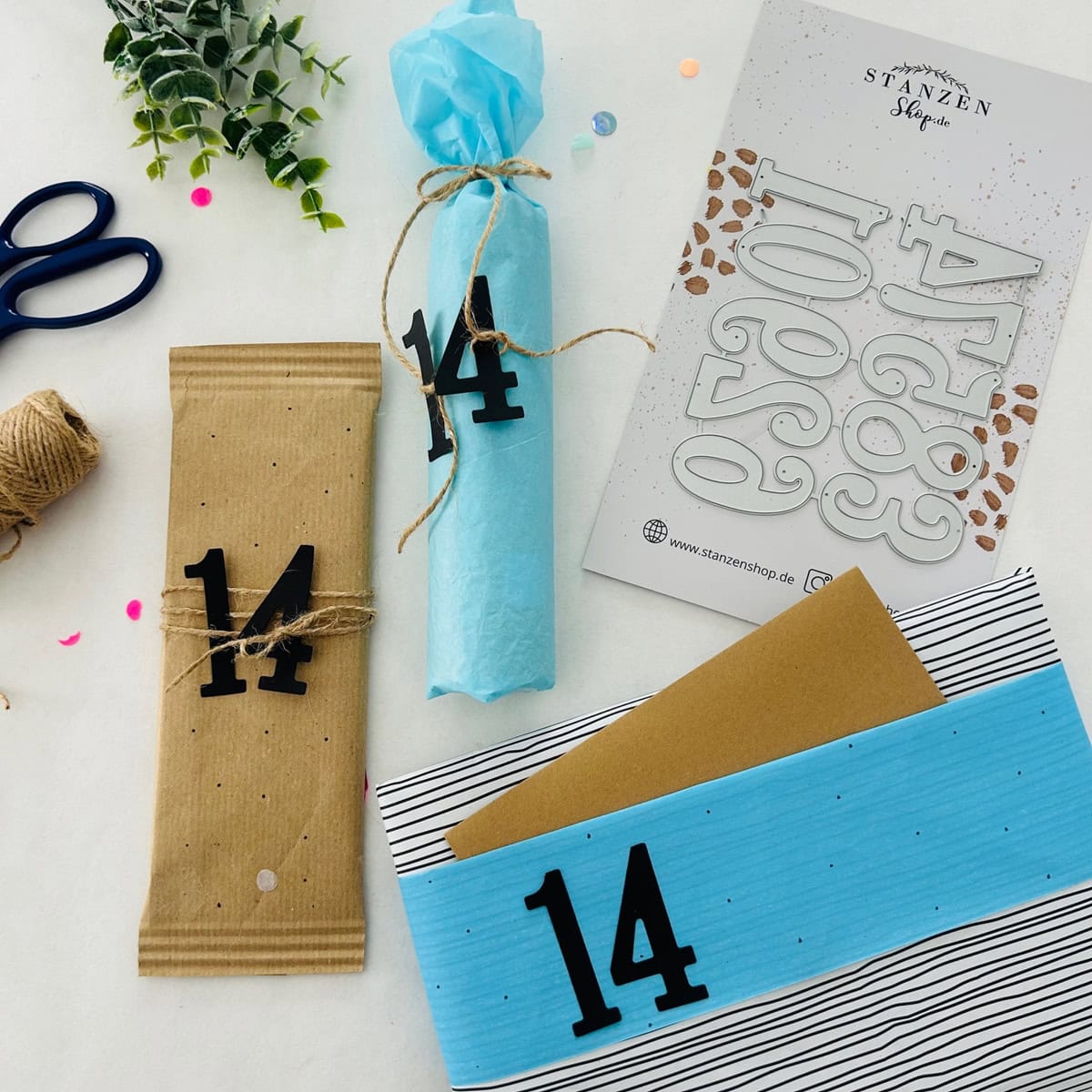 Drei Geschenkpakete mit blauem Seidenpapier, brauner Schnur, Schere und einem Stanzenschablone Große Zahlen Aufkleberbogen von Stanzenshop.de sind auf einer weißen Fläche angeordnet - ideal für Basteln oder Scrapbooking Projekte.