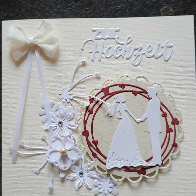 Eine handgefertigte Hochzeitskarte mit einer weißen Schleife, floralen Akzenten und der Silhouette des Brautpaares. Erstellt mit Stanzenshop.de's Stanzschablone Brautpaar, das Wort "Hochzeit" erscheint am oberen Rand.