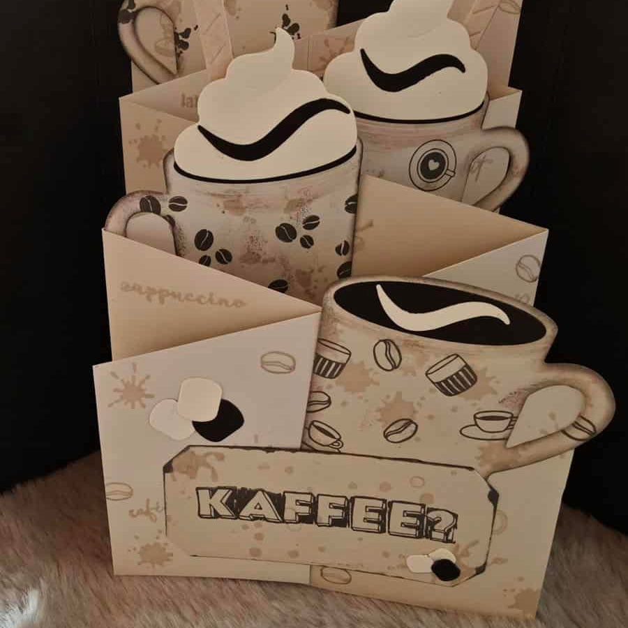 Eine handgefertigte Karte mit geschichteten Kaffeetassenausschnitten und "Kaffee" auf der Vorderseite, hergestellt mit der Stanzschablone: Tassen von Stanzenshop.de als kreatives Bastelzubehör, dargestellt auf einer pelzigen Oberfläche.