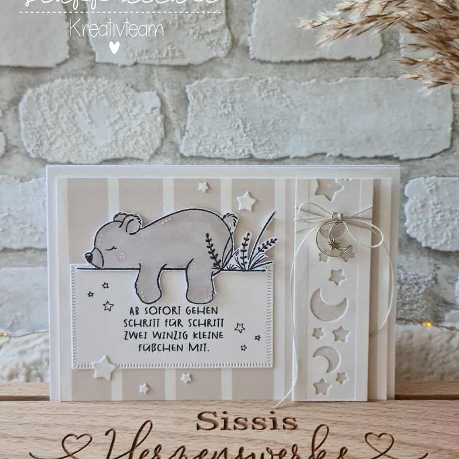Die "Stanzschablone: Mond /Sterneband" von Stanzenshop.de ist mit Mond- und Sternenmotiven versehen und eignet sich perfekt für Bastelprojekte. Abgebildet mit einer handgefertigten Karte mit Bärenmotiv, deutschem Text und dekorativer Kordel vor einer gemütlichen Backsteinmauer-Kulisse.
