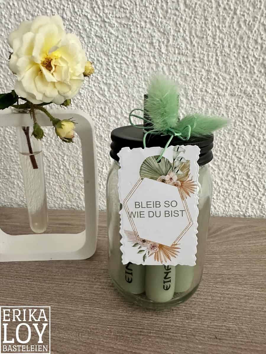 Die Stanzschablone "Sechs gewellte Rahmen in verschiedenen Größen" von Stanzenshop.de liegt neben einer weißen Vase mit gelber Blume-ideal zum Basteln oder Scrapbooking vor einer strukturierten weißen Wand.