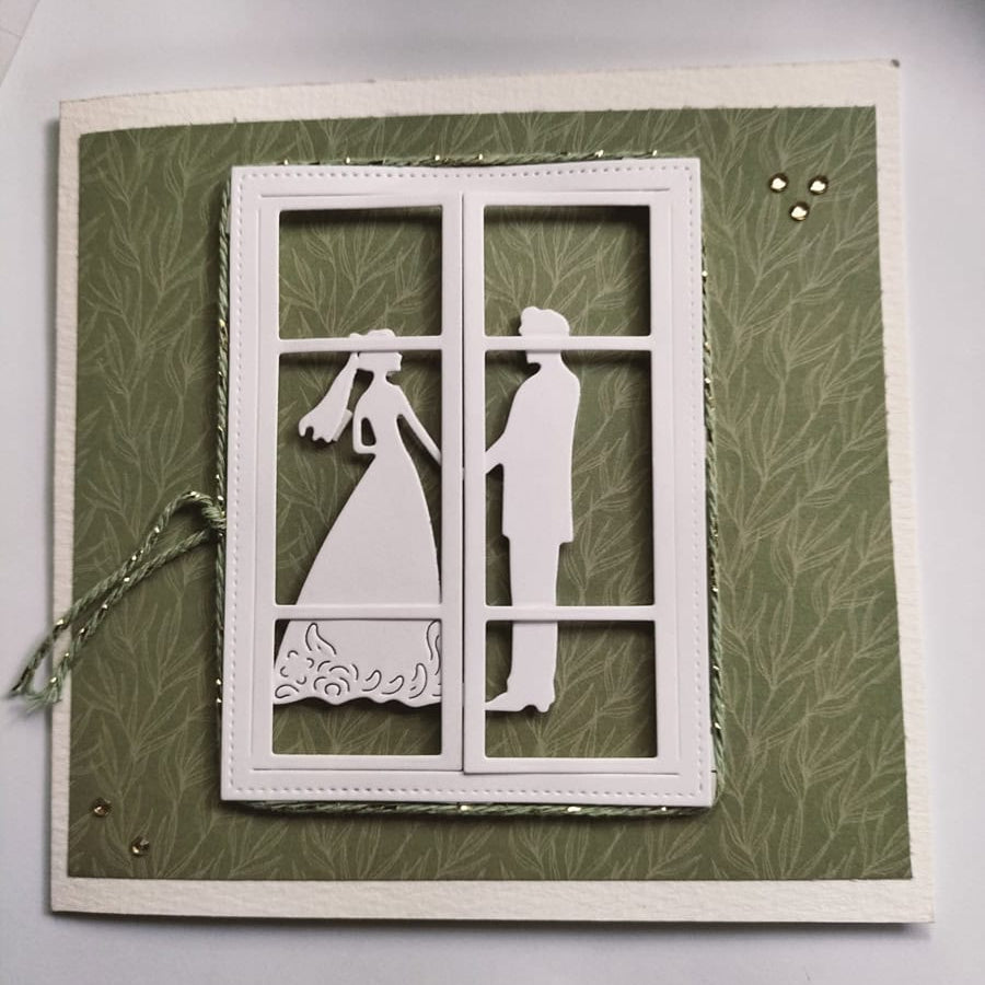 Eine Hochzeitskarte mit weißer Silhouette von Braut und Bräutigam, gefertigt mit der Stanzenshop.de Stanzschablone Brautpaar und umrahmt von einem Papierfenster auf grünem strukturierten Hintergrund - ideal für Basteln oder stilvolle Hochzeitseinladungen.