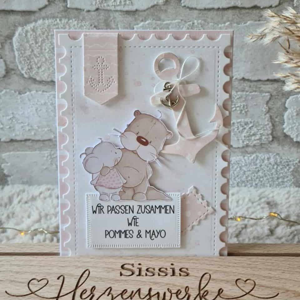 Eine handgefertigte Karte mit Cartoon-Bären, einem Anker und "Wir passen zusammen wie Pommes & Mayo" auf Deutsch, hergestellt mit Scrapbooking und der Stanzschablone Drei Briefmarken von Stanzenshop.de, steht auf einem "Sissis Herzenwerke" Holzblock.