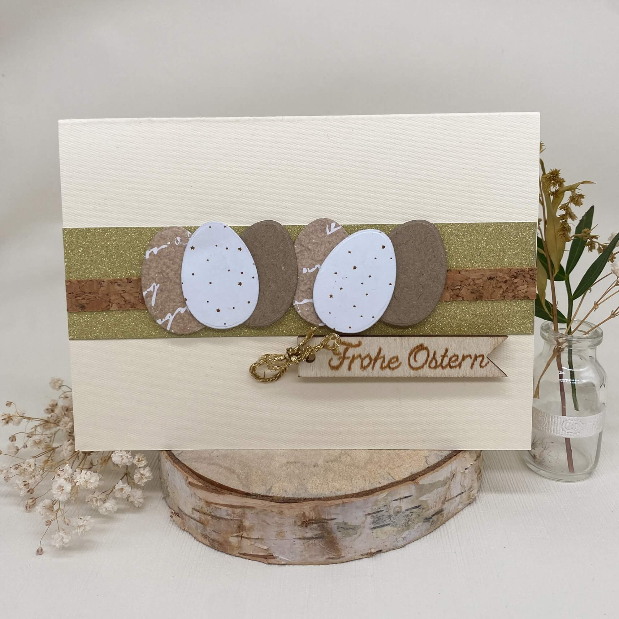 Eine handgemachte Osterkarte, dekoriert mit ovalen Motiven der "Stanzschablone Sechs Ostereier" von Stanzenshop.de und dem Schriftzug "Frohe Ostern", liebevoll arrangiert mit getrockneten Blumen sowie Glasvase - ideal für Basteln oder Scrapbooking.