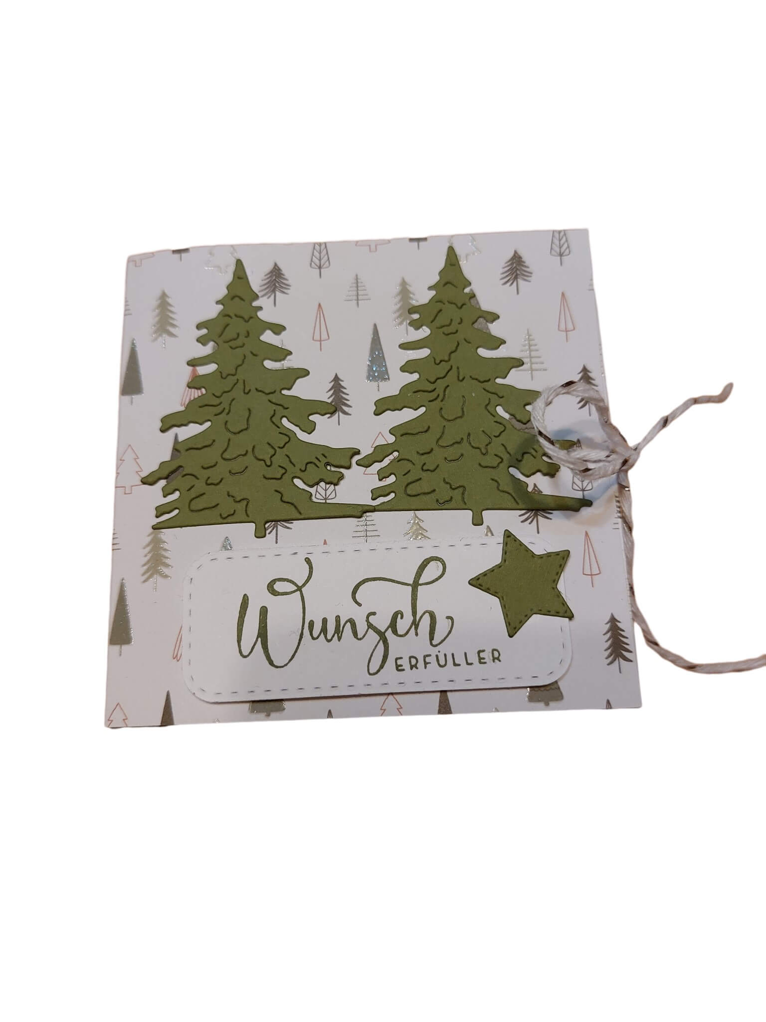 Eine quadratische Karte mit dem Motiv "Wunscherfüller", hergestellt mit der Stanzschablone von Stanzenshop.de: Drei Tannenbäume, verziert mit grünen gestanzten Bäumen, einem Stern und einer Schnurschleife auf einem baumgemusterten Hintergrund - ideal für winterliche Bastelarbeiten.