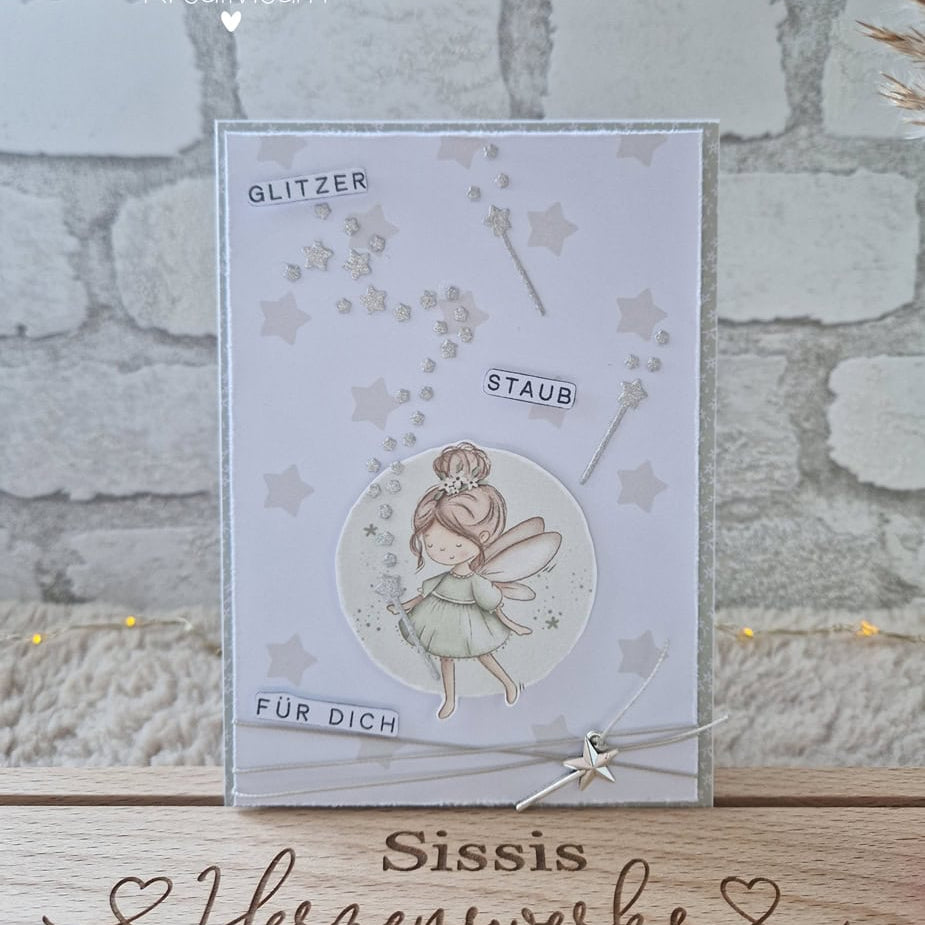 Eine handgefertigte Karte, die die Stanzschablone von Stanzenshop.de zeigt: Reihe aus Sternen und dem deutschen Text "Glitzer Staub für dich" - ein entzückendes Scrapbooking-Ergebnis - auf einem Holzständer mit der Aufschrift "Sissis Herzenswerke" präsentiert.