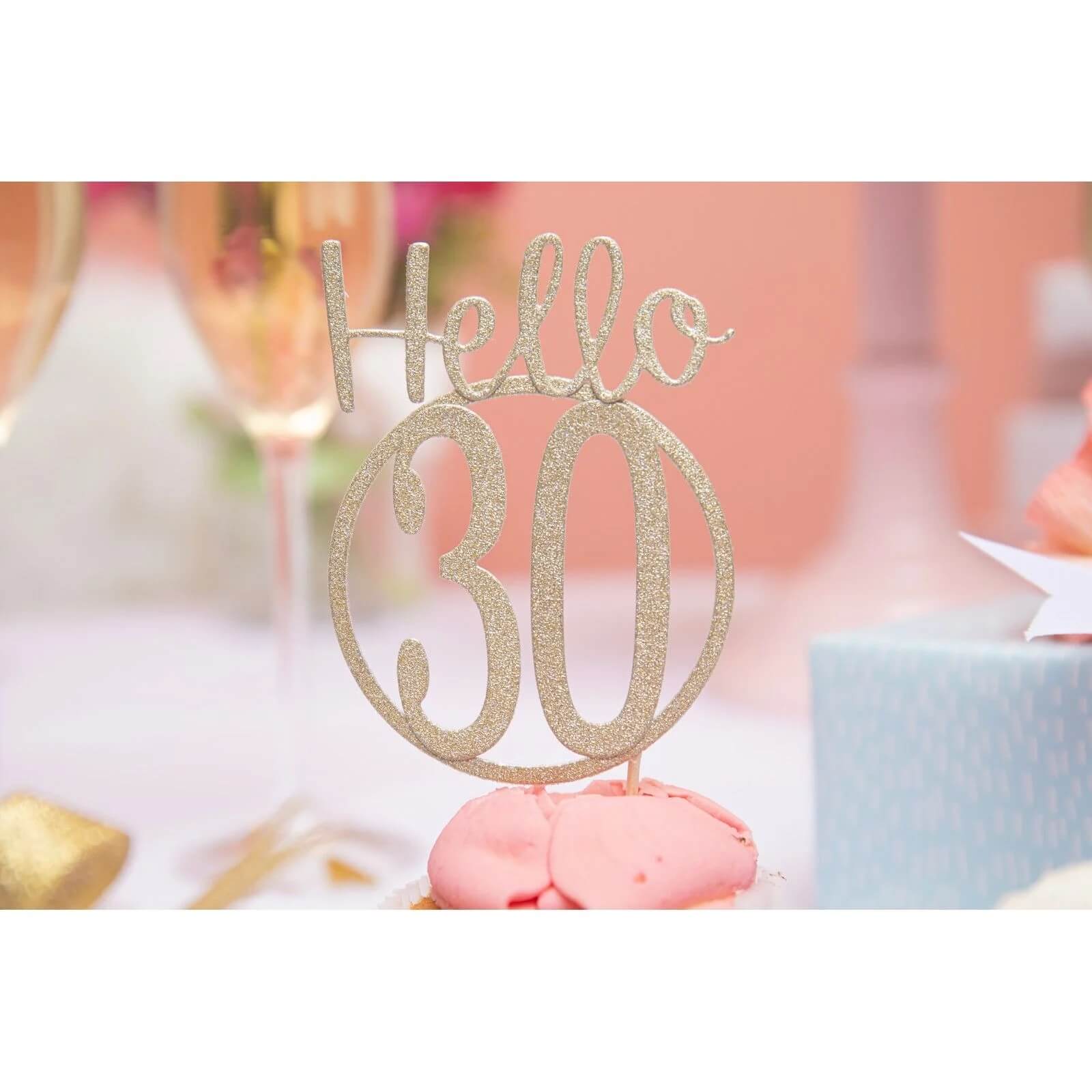 Sizzix 666230 - Thinlits Fabulous Birthday Numbers von Debi Potter Kuchentopper auf rosa Macarons, ideal für das Scrapbooking von Partyerinnerungen. Champagnergläser und eine blaue Geschenkbox erscheinen im verschwommenen Hintergrund. Marke: Sizzix.