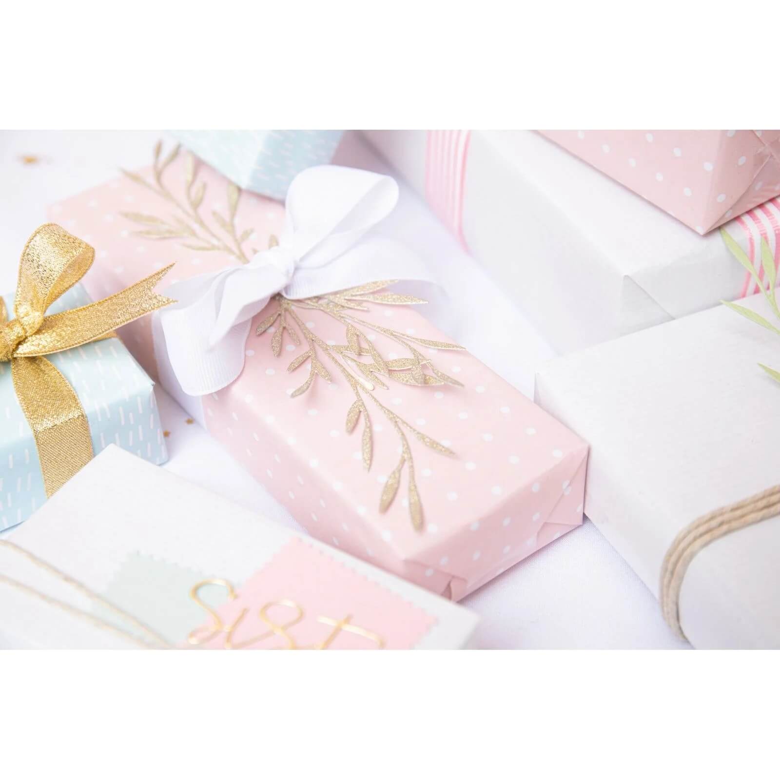 Mehrere pastellfarbene Geschenkschachteln, die sich perfekt für die Kartengestaltung oder das Scrapbooking eignen, sind zusammen angeordnet. Die rosa Schachtel mit weißer Schleife und goldenem Dekor ist eine tolle Inspiration für die Sizzix 666254 - Thinlits Woodland Stems von Olivia Rose von Sizzix.