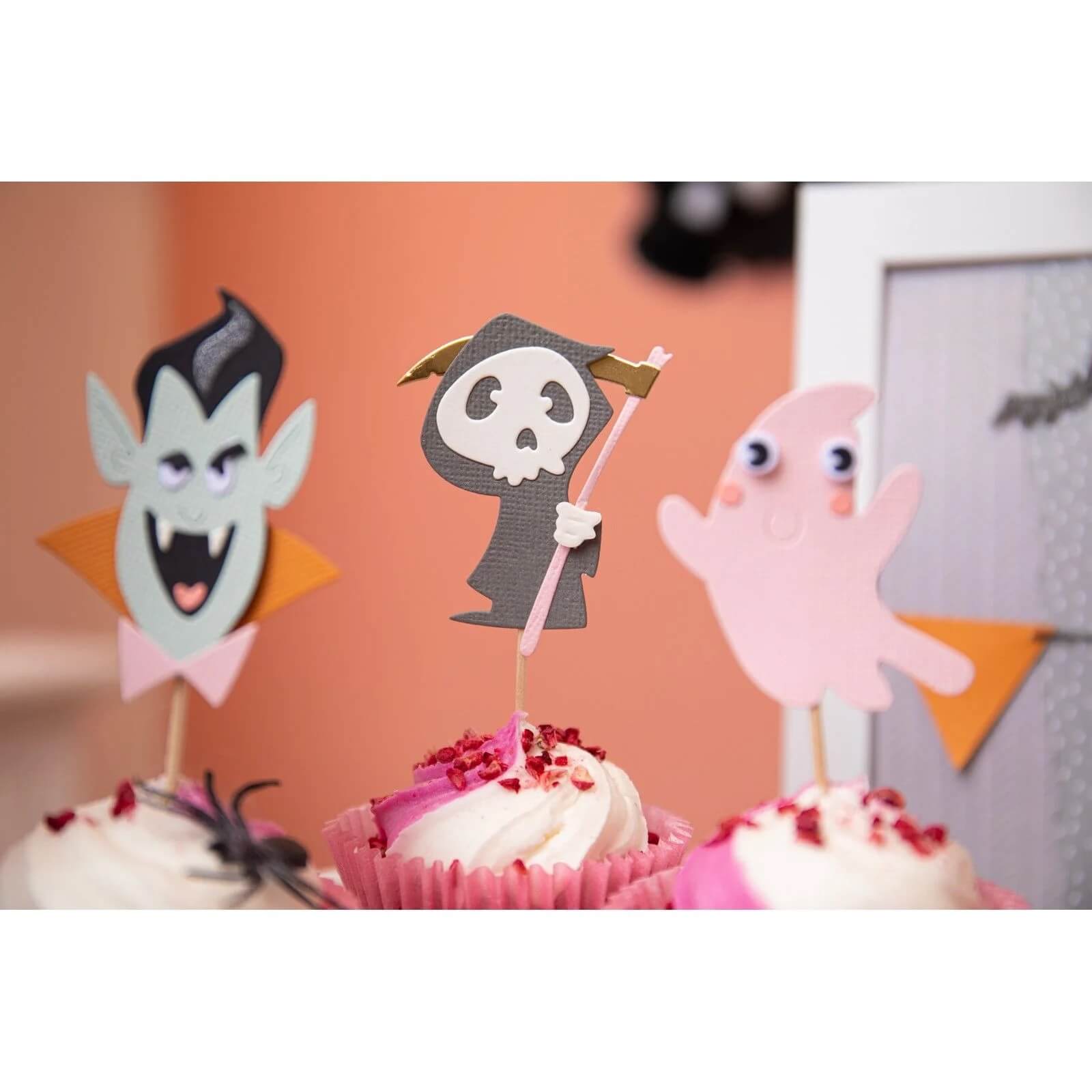 Drei Cupcakes mit Halloween-Figuren - Vampir, Sensenmann und Gespenst -, die mit den Sizzix 666315 Thinlits mit Stamps Spooky Friends von Sizzix hergestellt wurden; ideal für Papierbastelprojekte und gruselige Feiern.
