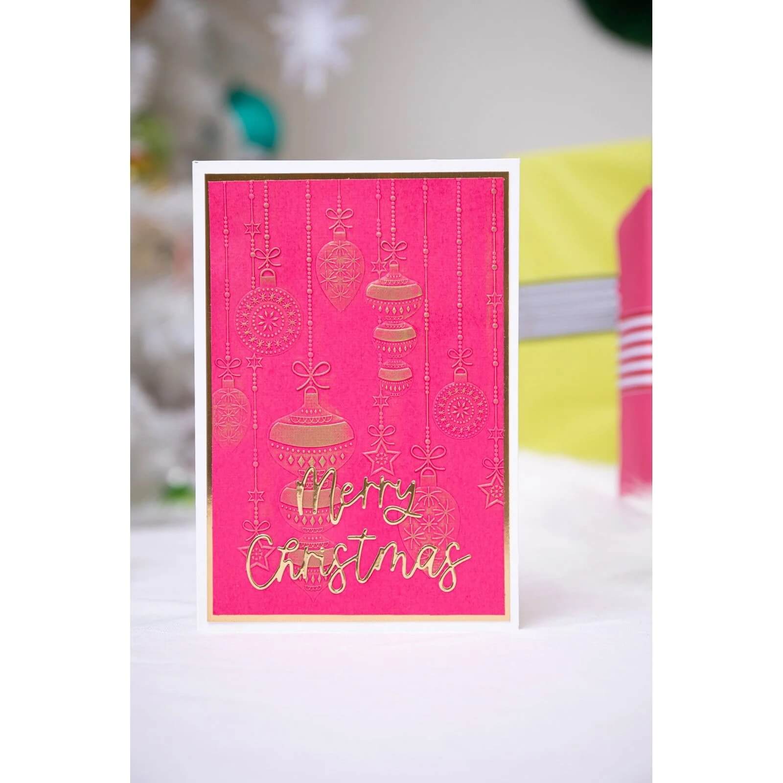 Die Sizzix 666457 - Thinlits Variety Sentiments #2 von Sizzix zaubert eine festliche rosa Weihnachtskarte mit goldenen Ornamenten und "Merry Christmas", perfekt für die Kartengestaltung oder als stilvolle Grußkarte für Weihnachten, aufrecht stehend auf einer weißen Fläche.