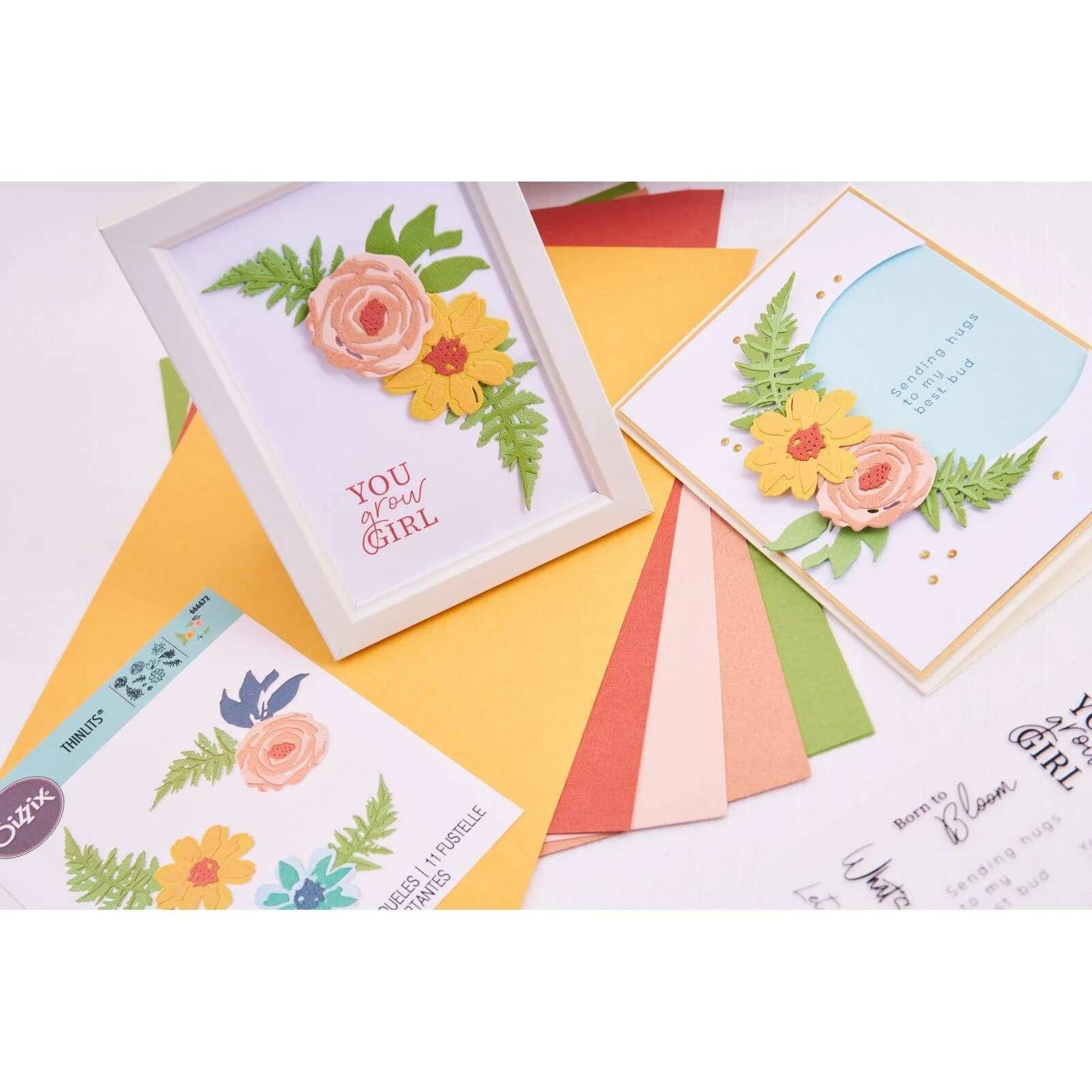 Handgemachte Blumengrußkarten auf farbigen Papierbögen, umgeben von Bastelmaterial, klaren Stempeln und den Sizzix 666672 Thinlits Flowers & Fern 11pcs Stanzen.
