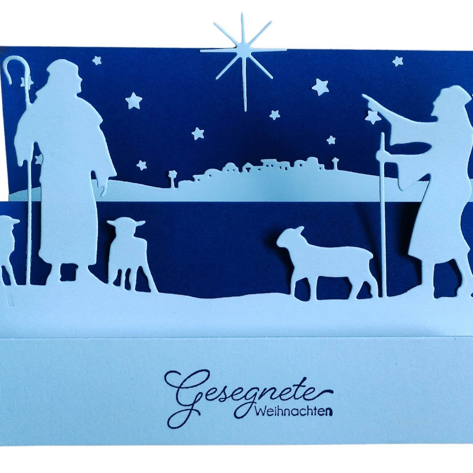 Eine Papier-Weihnachtskarte mit der "Stanzschablone Hirten" von Stanzenshop.de zeigt eine Krippensilhouette mit Hirten, Schafen und einem Stern, dazu den Text "Gesegnete Weihnachten". Perfekt für Kartenherstellung und Basteln von Wintermotiven.