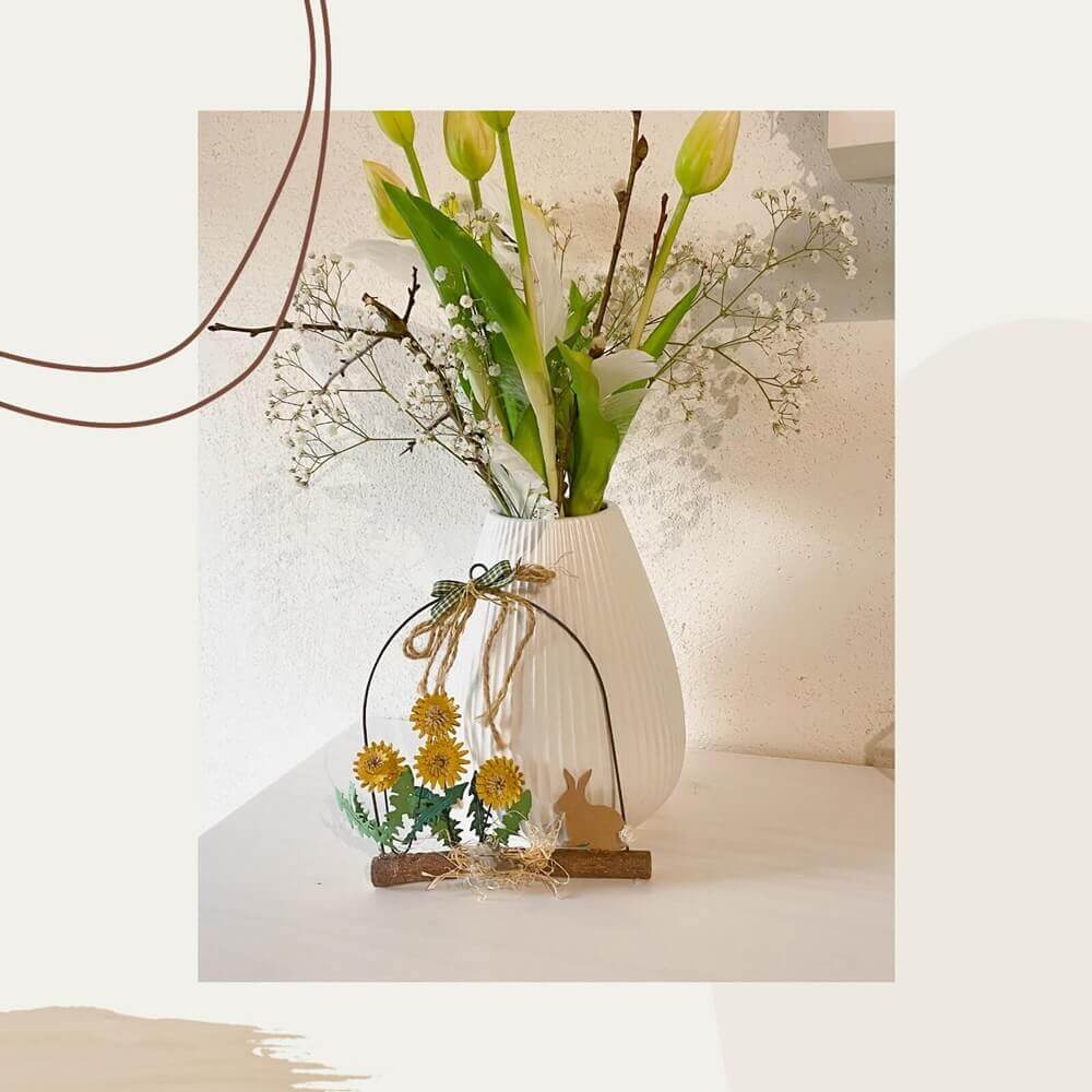 Eine weiße Vase mit Lilien und Schleierkraut steht neben einer kleinen Holzdekoration mit gelben Blumen, einer Häschensilhouette und dem Stanzschablone Bastelset Löwenzahn von Stanzenshop.de zum Scrapbooking oder Basteln.