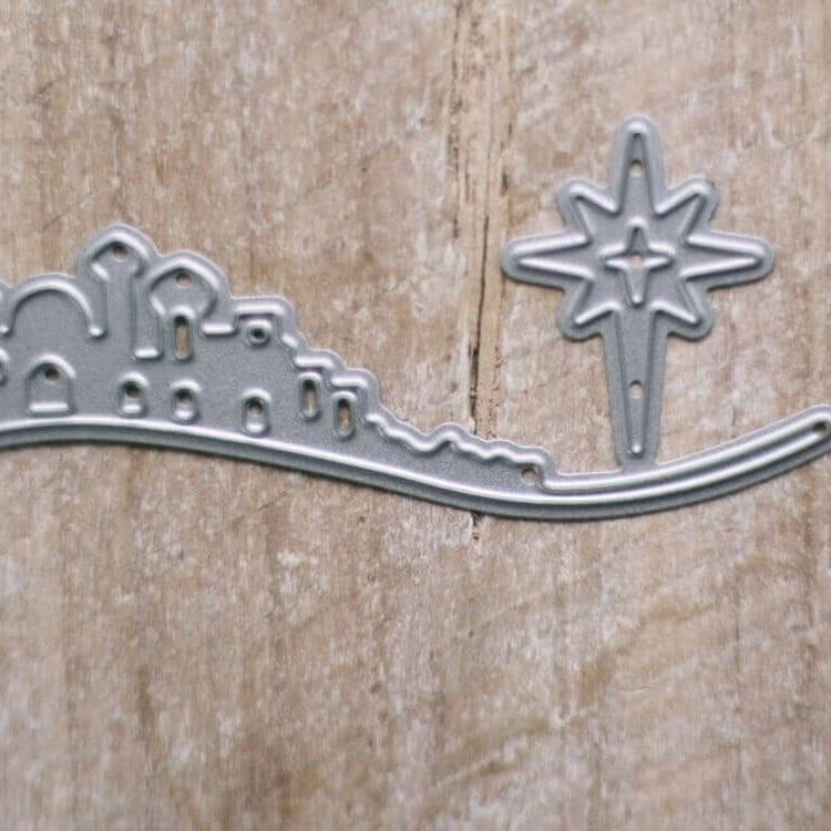 Die Stanzenshop.de Stanzschablone "Bethlehem mit Weihnachtsstern" zeigt eine kleine Stadtsilhouette mit einem großen Stern, ideal für Kartenherstellung oder Basteln im Winter, dargestellt auf einem Holzhintergrund.