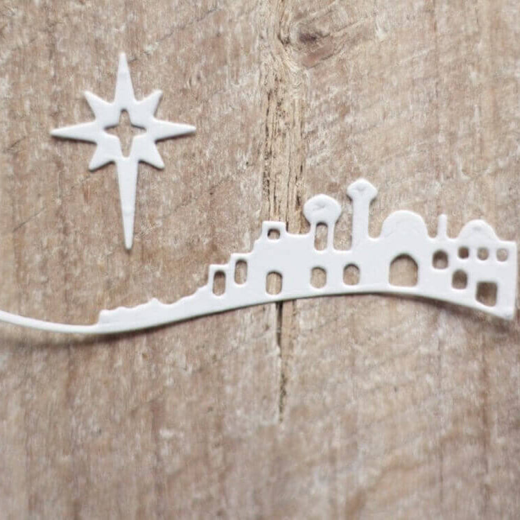 Die "Stanzschablone: Bethlehem mit Weihnachtsstern" von Stanzenshop.de zeigt ein weißes Stadtbild und den Stern von Bethlehem auf strukturiertem Holz, perfekt für Winterbasteln oder Kartengestaltung in Ihren liebsten Weihnachtsprojekten.