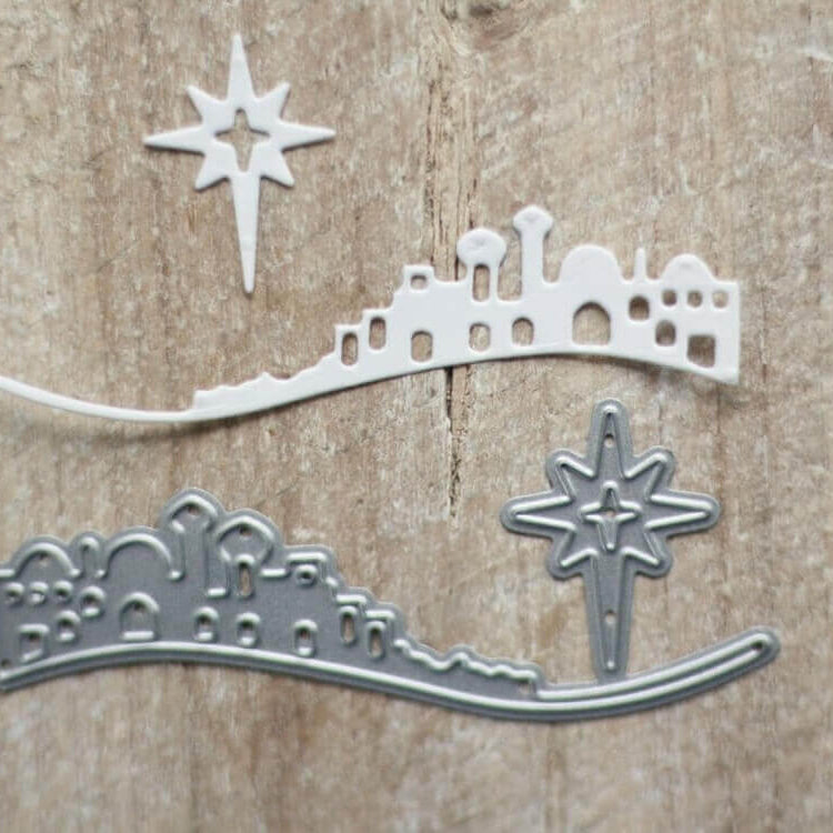 Zwei gestanzte Formen - eine Skyline von Bethlehem und ein Weihnachtsstern, eine weiß und eine metallisch - sind auf Holz abgebildet, ideal für kreative Kartenherstellung oder Basteln im Winter mit Ihrer Stanzschablone: Bethlehem mit Weihnachtsstern von Stanzenshop.de.