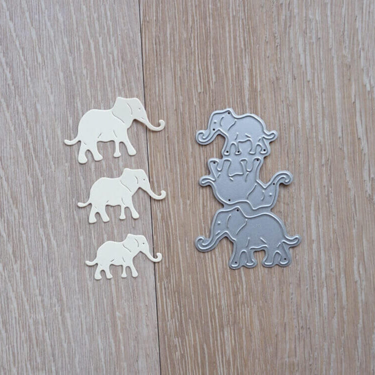 Vier cremefarbene Papierelefanten liegen neben drei gestapelten Stanzschablonen Drei Elefanten von Stanzenshop.de auf einer Holzfläche - ideal zum Basteln oder für Scrapbooking-Projekte.