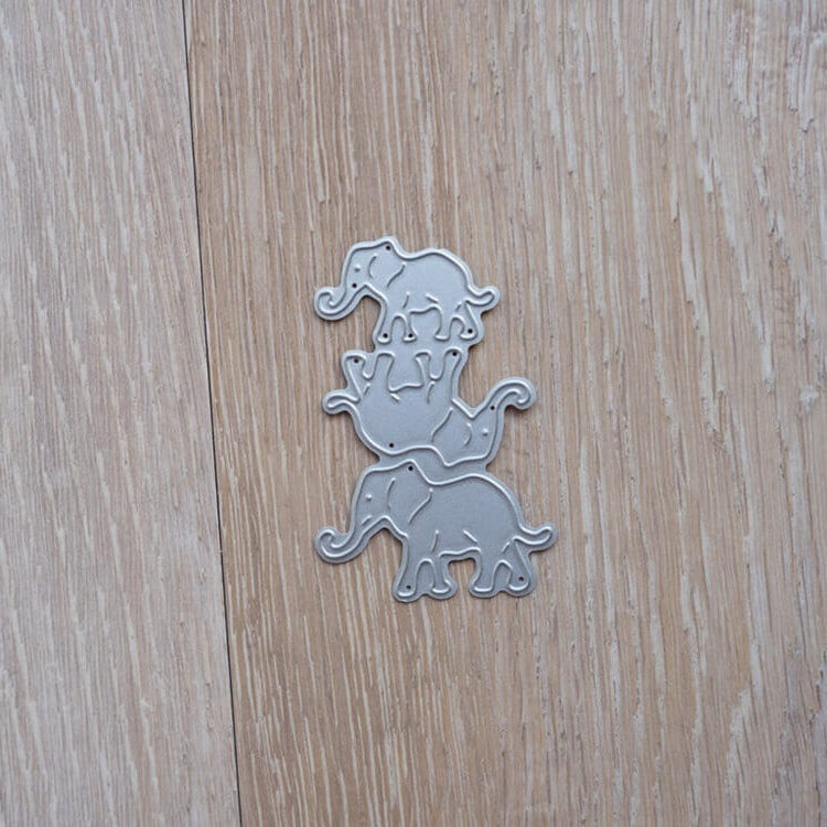Drei silberne Elefantenausschnitte aus der Stanzschablone Drei Elefanten von Stanzenshop.de sind auf einer hellen Holzfläche gestapelt - ideal für Scrapbooking- oder Bastelprojekte.