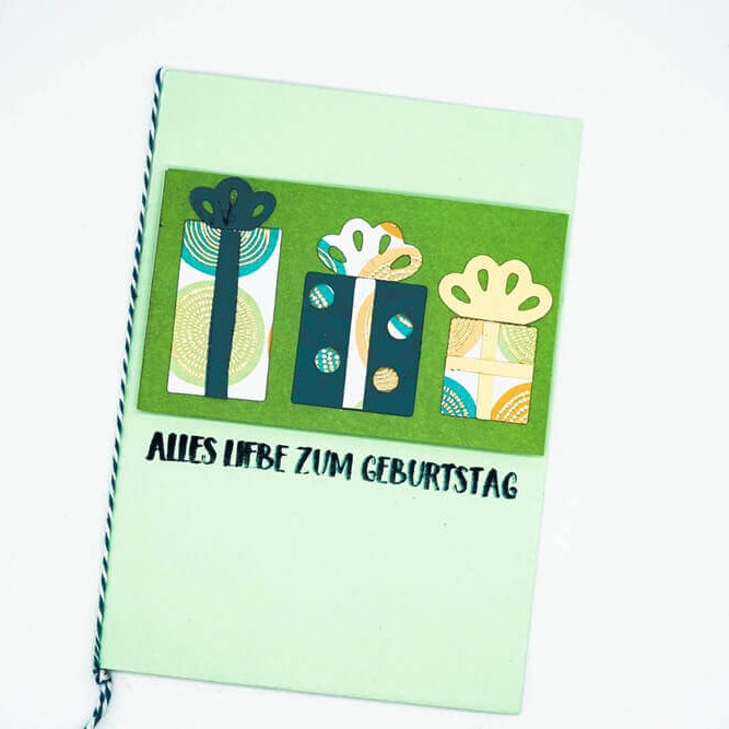 Eine hellgrüne Karte von Stanzenshop.de, gestaltet mit der Stanzschablone "Drei verschiedene Geschenke" und dem Text "ALLES LIEBE ZUM GEBURTSTAG" unter den illustrierten Geschenkboxen.