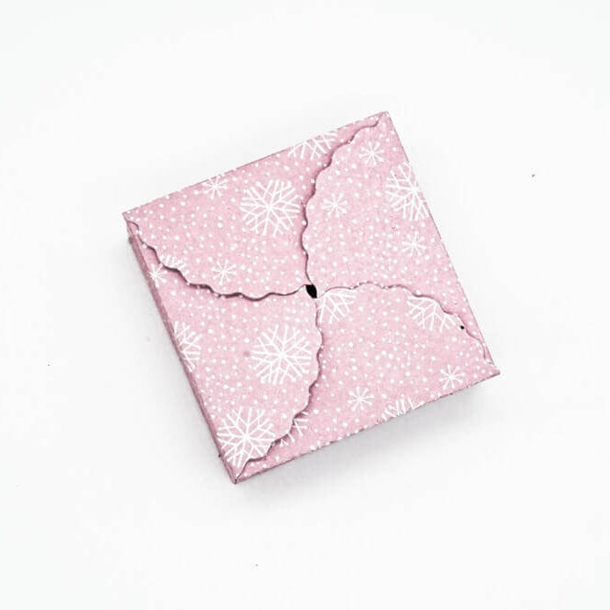 Die Stanzschablone Geschenkkästchen von Stanzenshop.de zeigt einen geschlossenen rosa Umschlag mit Schneeflockenmuster und Wellenkanten, perfekt zum Basteln oder Scrapbooking, abgebildet auf einem weißen Hintergrund.