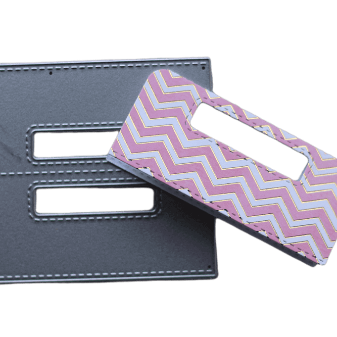 Zwei rechteckige Lederstücke - eines einfarbig grau, eines mit einem rosa, lila und gelben Zickzackmuster - sind mit ausgeschnittenen Griffen und Nähten versehen. Ideales Bastelergebnis für Scrapbooking oder zum Kombinieren mit der Stanzschablone Griffe von Stanzenshop.de.