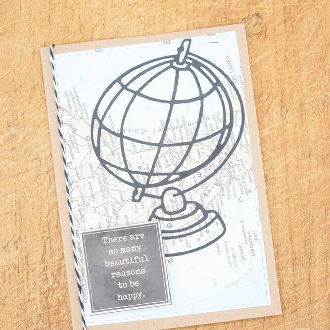 Die "Stanzschablone: Großer Globus" von Stanzenshop.de ist eine Grußkarte im Globus-Design mit der Botschaft "Es gibt so viele schöne Gründe, glücklich zu sein", dargestellt auf einer Holzoberfläche - ideal für Scrapbooking.