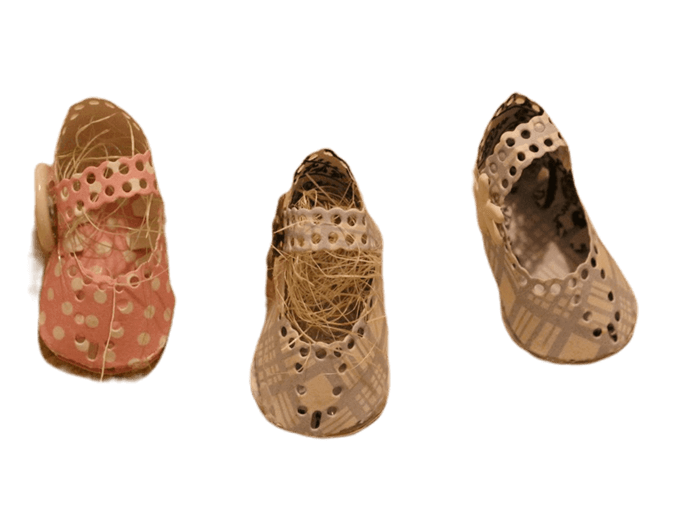 Drei handgefertigte, gewebte Babyschuhe mit perforierten Mustern sind auf weißem Hintergrund abgebildet - links rosa, in der Mitte strohgelb, rechts beige - eine ideale Inspiration für Ihre Projekte mit der Stanzschablone Kinderschuh für ein Baby von Stanzenshop.de.