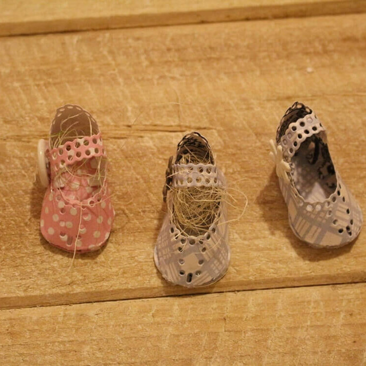 Drei kleine, handgefertigte Puppenschuhe - rosa mit weißen Tupfen und blauen Mustern - sitzen auf Holz und bieten Inspiration für die Verwendung der Stanzenshop.de Stanzschablone Kinderschuh für ein Baby in Ihrem nächsten Scrapbooking-Projekt.