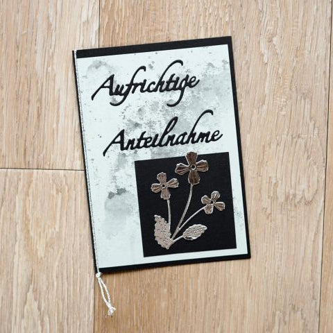 Eine Kondolenzkarte mit "Aufrichtige Anteilnahme" und der Stanzenshop.de Stanzschablone: Kleine Blume mit drei Blüten Design, ideal zum Basteln oder Scrapbooking, liegt auf einer Holzunterlage.