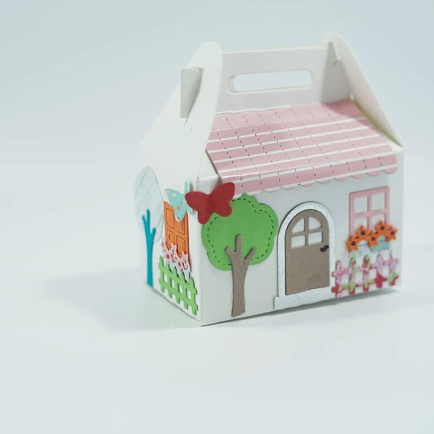 Charmante kleine Geschenkbox aus Pappe in Form eines Hauses mit rosa Dach, Bäumen, Schmetterling und Blumen - perfekt zum Osterbasteln mit der "Stanzschablone: Osterset" von Stanzenshop.de.