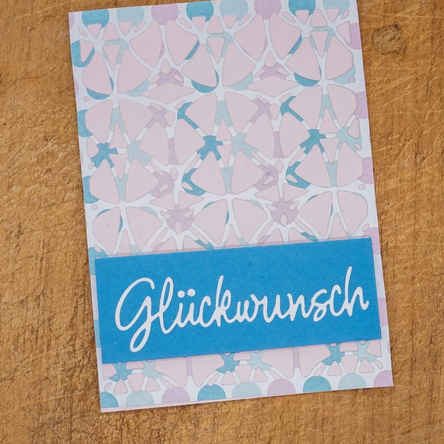 Die Stanzschablone "Platte mit Kreismuster" von Stanzenshop.de gestaltet eine pastellfarbene geometrische Karte mit blauem Rechteck und "Glückwunsch" in weißer Schrift - ideal für Kartenherstellung und kreative Anlässe.