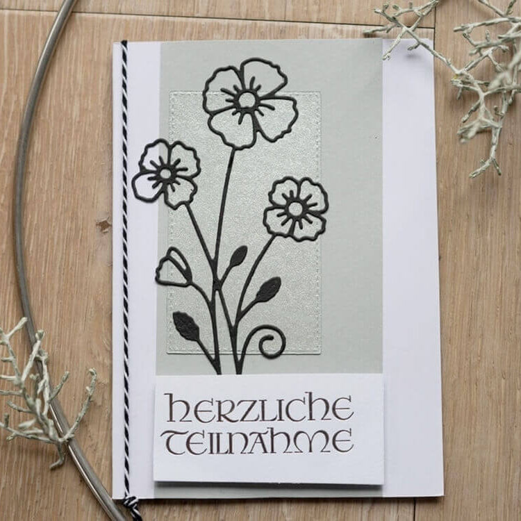 Eine Beileidskarte für Basteln Karten & Scrapbooking mit schwarz umrandeten Blumen, dem Text "Herzliche Anteilnahme" und der Stanzschablone Rechteckige Rahmen von Stanzenshop.de in sieben Größen, dargestellt auf Holz mit getrockneten Pflanzen.