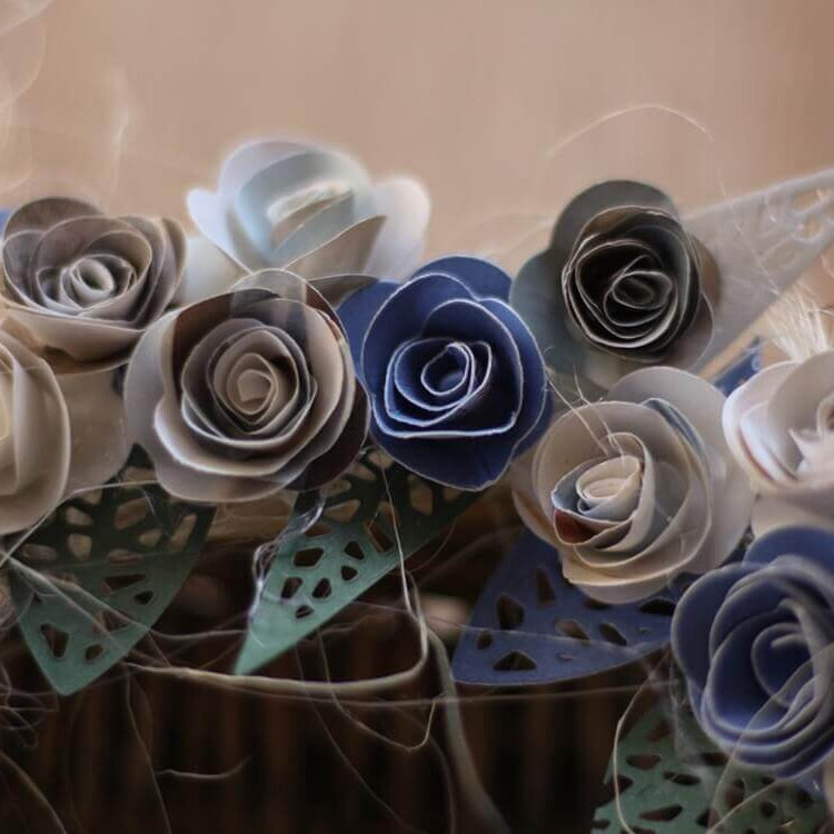Eine Nahaufnahme von blauen, weißen und grauen Papierrosen mit verschlungenen Blütenblättern, hergestellt mit der Stanzschablone Rosenblüte von Stanzenshop.de - perfekt für Scrapbooking und kreative Arrangements.