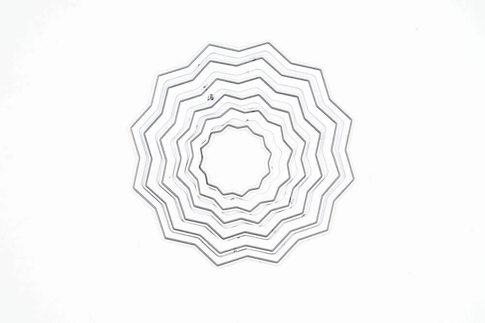 Eine Reihe konzentrischer, zickzackförmiger Ringe in einem kreisförmigen Muster auf Weiß - ideal für kreative Projekte mit der Stanzschablone: Rosette 6-teilig von Stanzenshop.de.