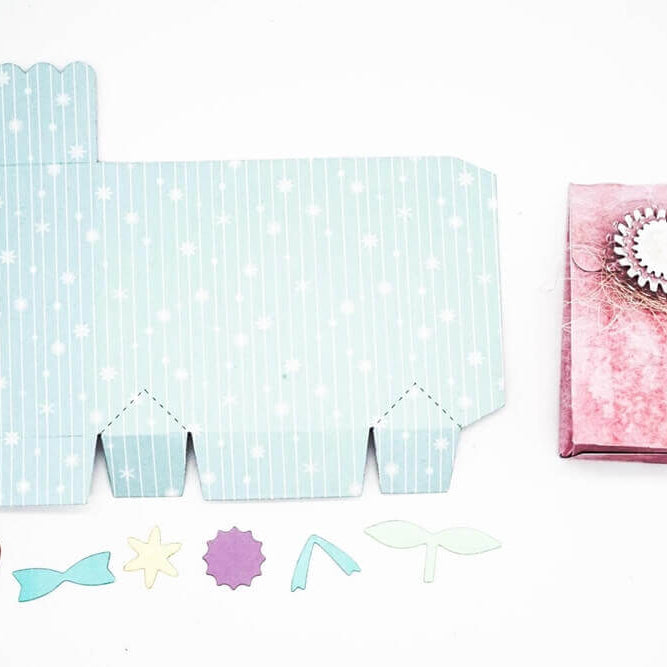 Gestalten Sie mit der Stanzschablone Schachtel mit Verzierungen von Stanzenshop.de individuelle Partygeschenke: Basteln Sie eine flache gemusterte Schachtel, schneiden Sie dekorative Formen aus und fügen Sie eine bezaubernde Geschenkschachtel aus rosa Papier mit einem einzigartigen Siegel zusammen.