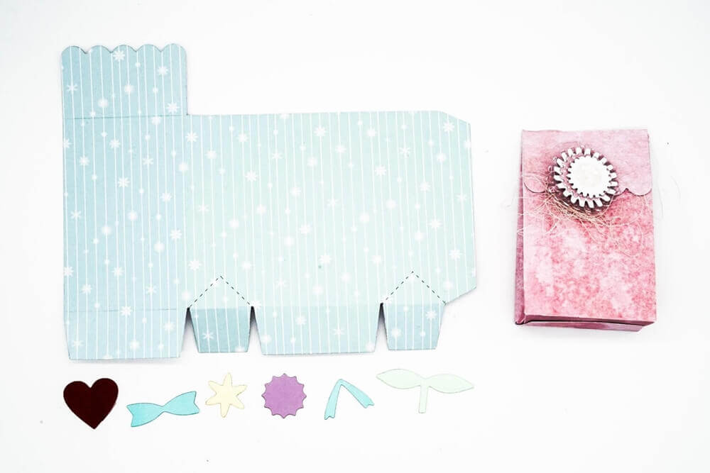 Gestalten Sie mit der Stanzschablone Schachtel mit Verzierungen von Stanzenshop.de individuelle Partygeschenke: Basteln Sie eine flache gemusterte Schachtel, schneiden Sie dekorative Formen aus und fügen Sie eine bezaubernde Geschenkschachtel aus rosa Papier mit einem einzigartigen Siegel zusammen.