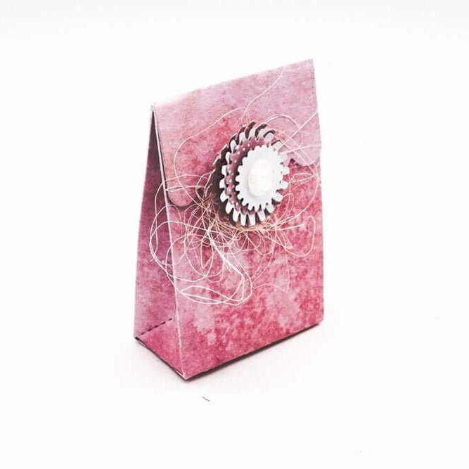 Eine kleine rosa Geschenktüte, verziert mit einer Blume aus der Stanzschablone Schachtel mit Verzierungen von Stanzenshop.de und Kordel auf der Vorderseite, perfekt für Gastgeschenke, dargestellt auf weißem Hintergrund.