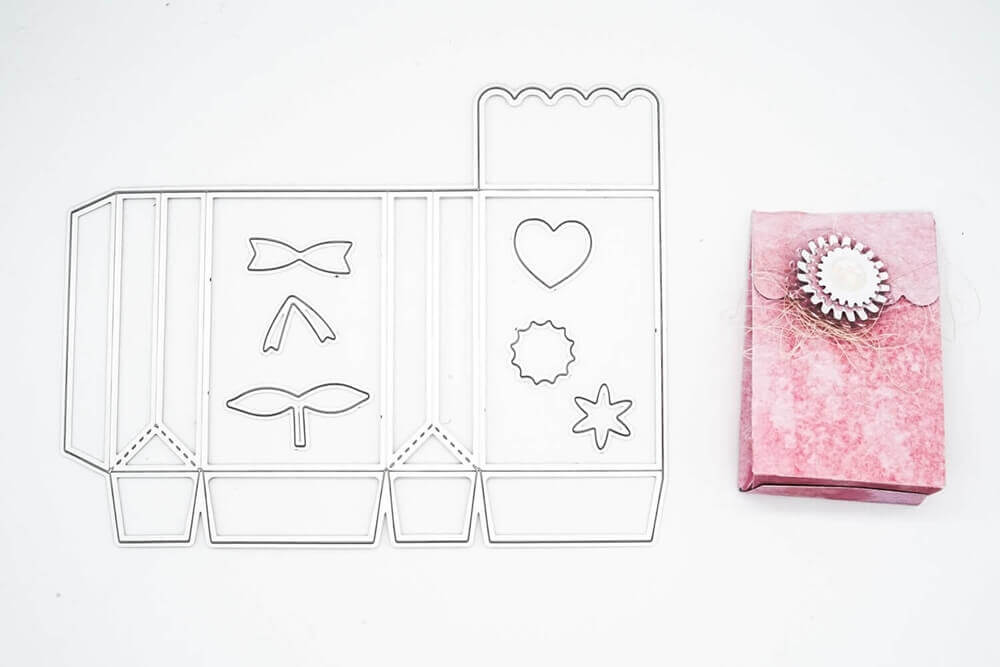 Die Stanzschablone Schachtel mit Verzierungen von Stanzenshop.de liegt neben einer rosafarbenen Geschenkbox mit kreisförmiger Verzierung - ideal zum Schachtel basteln oder zum Basteln von einzigartigen Gastgeschenken.